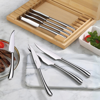 
                    
                      Set of eight stainless steel steak knives with curved handles, displayed in a bamboo storage box and on a marble surface.
                    
                  
