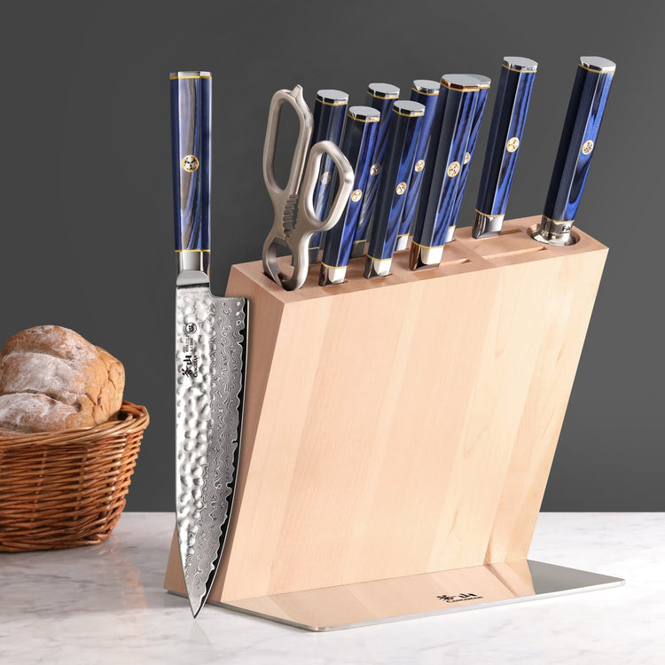Knife block set with eight knives and kitchen scissors, featuring blue handles and a wooden block on a countertop.