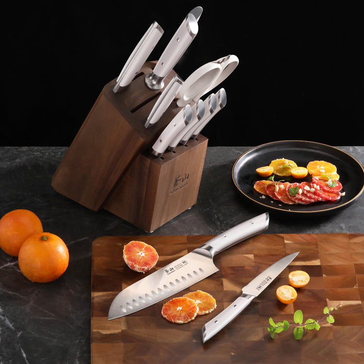 12-piece knife set with white handles in acacia wood block, two knives on cutting board with sliced citrus fruits.