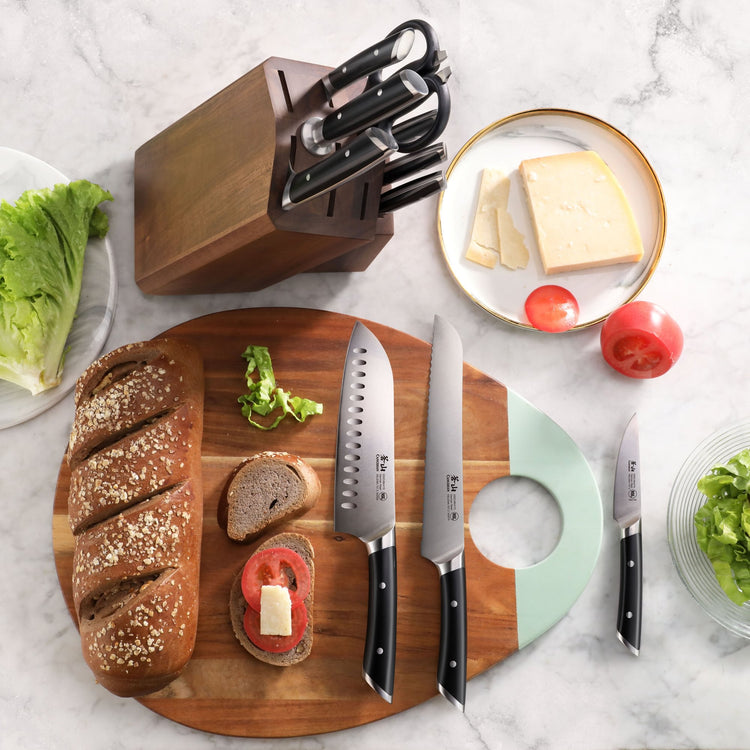 Wooden knife block with six knives, three knives on a cutting board with bread, tomato, and lettuce, and a plate with cheese