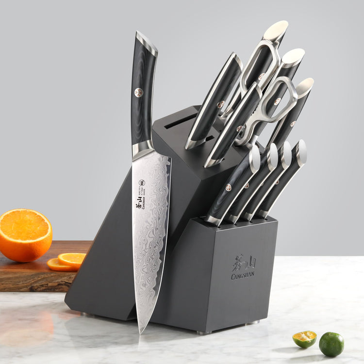 12-piece knife set with black handles in a black angled block, including scissors, displayed on a marble surface.