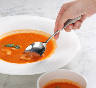 
                    
                      Hand holding a stainless steel spoon with matte finish handle scooping tomato soup from a white bowl.
                    
                  