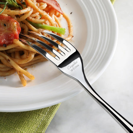 Fork resting on a white plate with spaghetti, tomato, and green vegetable on a green cloth.
