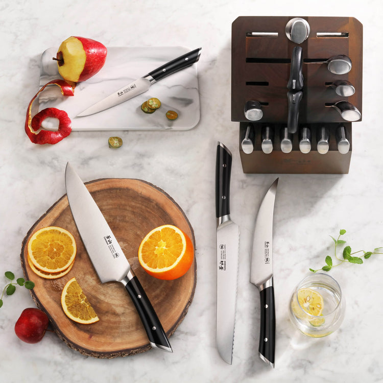 Knife block set with various knives, kitchen shears, and a sharpener displayed with sliced fruit on a marble surface.