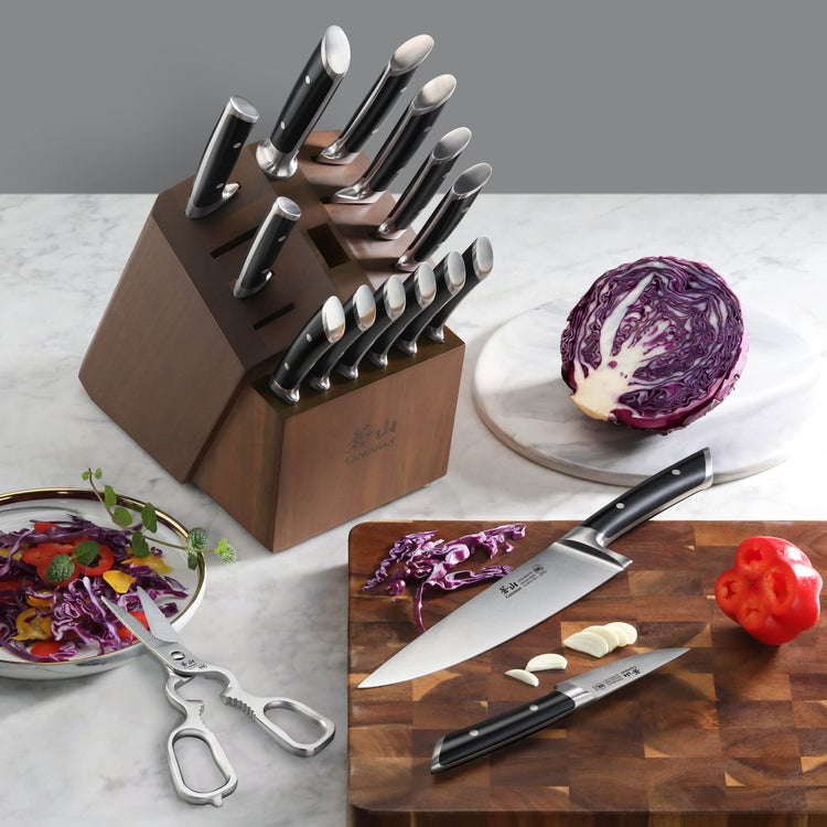 Wood block holding 17 black-handled knives with German steel blades, next to cut red cabbage, garlic, and a red bell pepper.