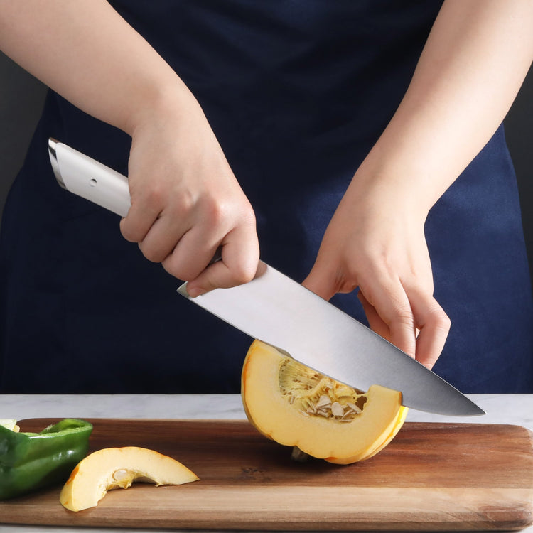 Person slicing a yellow squash on a wooden cutting board with a large kitchen knife.