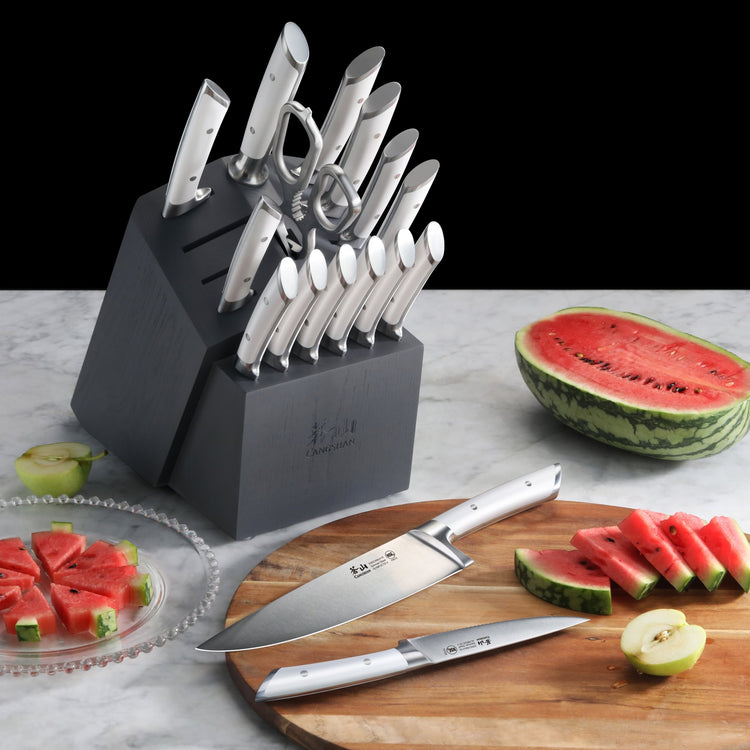 Knife block set with stainless steel knives, kitchen shears, and sharpening rod on a marble surface with sliced watermelon an