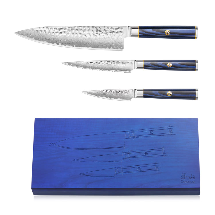 Three Damascus steel knives with hammered blades and blue handles, displayed above a matching blue wooden storage block.