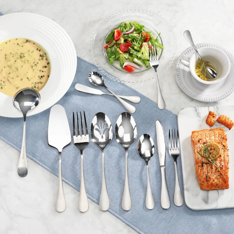 Set of stainless steel flatware with matte finish handles displayed on a blue cloth, including a slotted serving spoon.