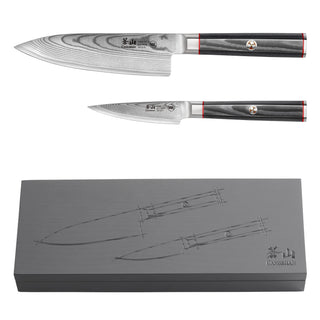 
                    
                      Two Damascus steel knives with dark handles and red accents, displayed above a gray box featuring etched knife illustrations.
                    
                  