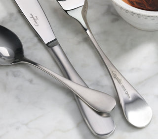 
                    
                      Three stainless steel flatware pieces with matte finish handles on a marble surface near a bowl.
                    
                  