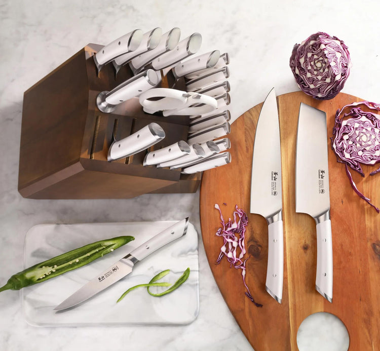 23-piece knife set with stainless steel blades and white handles in an acacia wood block, displayed with sliced vegetables.