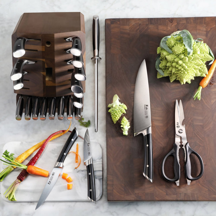 23-piece knife set with wooden block, sharpening steel, kitchen scissors, and vegetables on cutting boards.