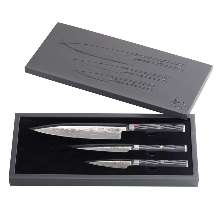 Three knives with patterned blades and black handles in a black box with a gray lid featuring knife sketches.