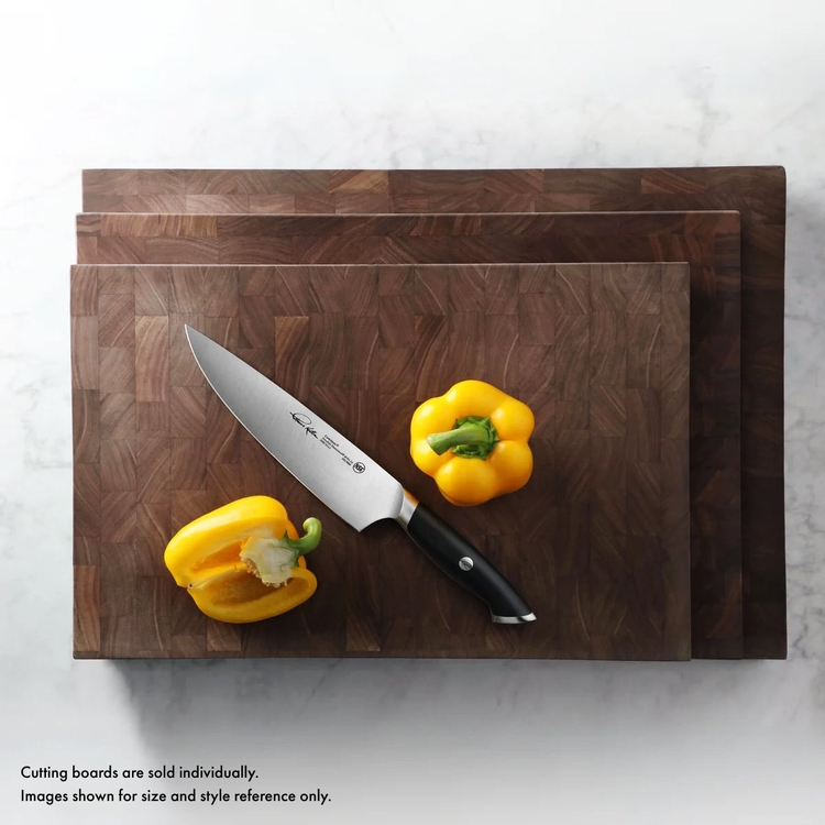 Three stacked walnut end-grain cutting boards with a chef's knife and two yellow bell peppers on the top board.