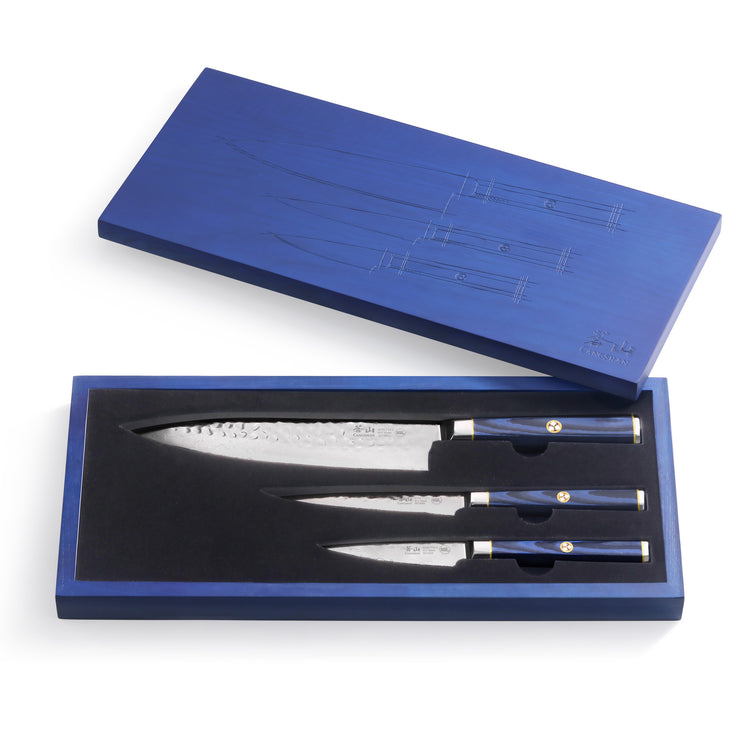 Three Damascus steel knives with blue handles in a blue wooden box with a matching lid.