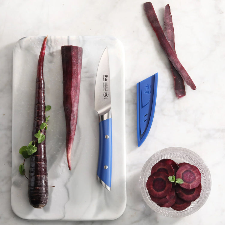 Paring knife with blue handle and sheath on marble board next to whole and sliced purple carrots and a bowl of carrot slices.