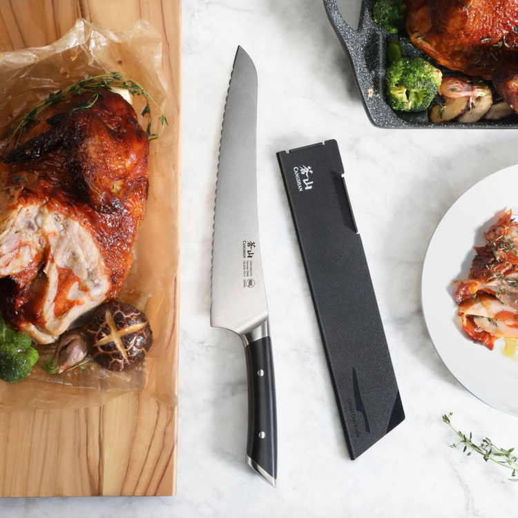 9-inch black-handled serrated deli knife with protective sheath next to roasted chicken and vegetables.