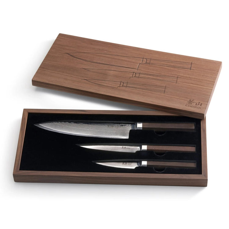 Three Damascus steel knives with dark handles in a wooden box with a lid featuring knife outlines.