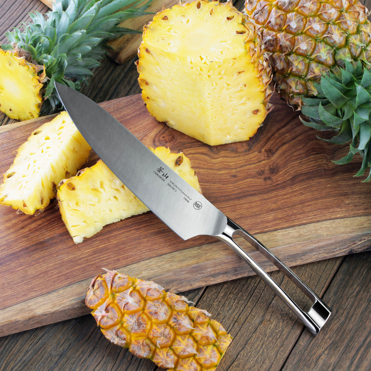 Chef's knife with stainless steel handle on wooden cutting board with sliced pineapples.