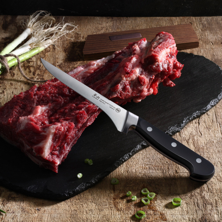 Raw beef ribs on a black slate board with a boning knife resting on top, green onions nearby.
