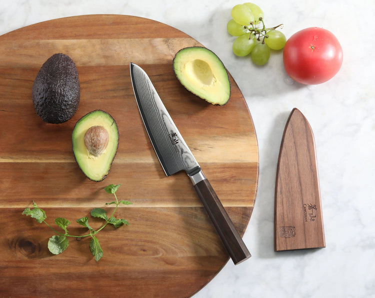 MAYA 5.5-Inch Prep Utility Knife with Damascus steel blade and wooden sheath on a cutting board with avocados.