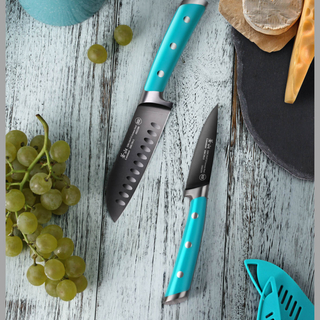 
                    
                      Two turquoise-handled knives on a wooden surface, next to grapes and cheese on a black slate board.
                    
                  