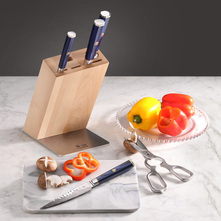 Wooden knife block with four knives, a cutting board with sliced mushrooms and bell pepper, kitchen shears, and whole bell pe