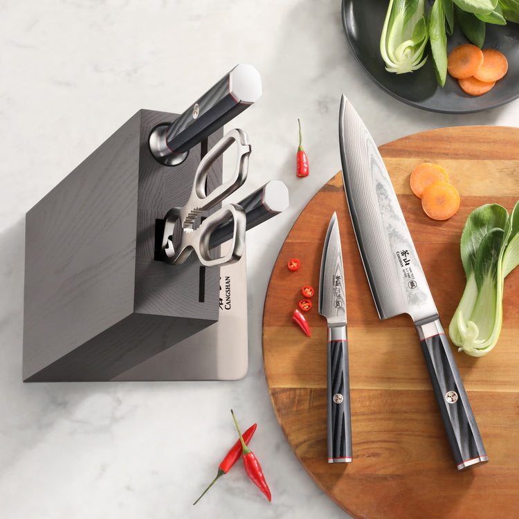 Six-piece knife block set with two knives, kitchen scissors, and a black wooden block on a marble countertop next to a cuttin
