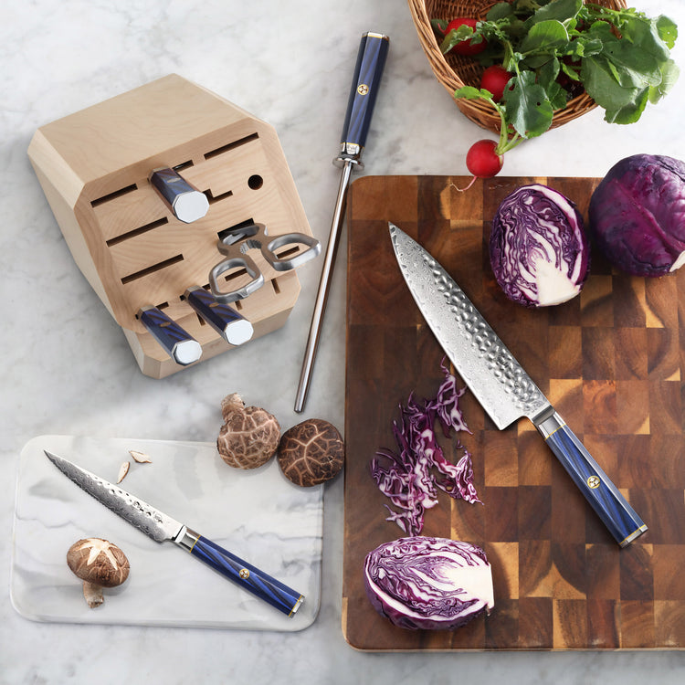 Wooden knife block with empty slots and blue-handled knives, including a chef's knife on a cutting board with chopped purple