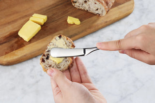 
                    
                      Person spreading butter on a slice of bread using a small stainless steel butter knife.
                    
                  