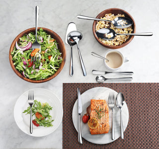 
                    
                      Serving spoon with mirror finish placed in wooden bowls with salad and cereal, alongside plated salad and salmon meal with fl
                    
                  