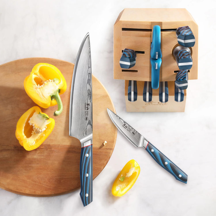 Wooden knife block with blue-handled knives, two knives on a cutting board with halved yellow bell pepper.