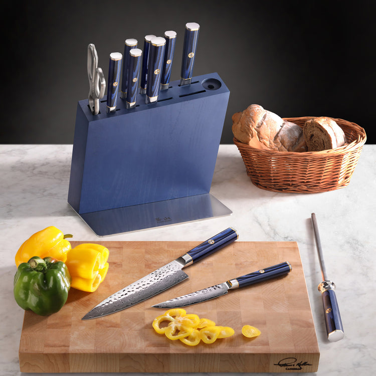Blue knife block set with six knives, kitchen shears, and sharpening rod, two knives on cutting board with sliced yellow bell