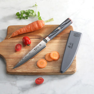
                    
                      Serrated utility knife with black handle and sheath on wooden board, alongside sliced carrot, whole carrot, and cherry tomato
                    
                  