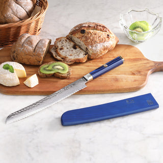 
                    
                      9-inch serrated bread knife with blue handle and sheath on wooden board with sliced bread, cheese, and kiwi.
                    
                  