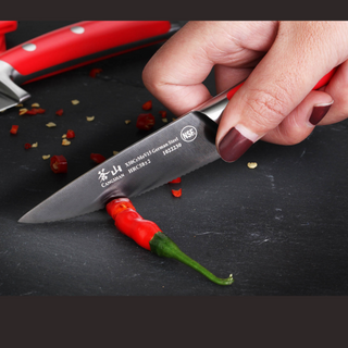 
                    
                      Hand with dark red nail polish slicing a red chili pepper on a black surface using a small serrated knife.
                    
                  