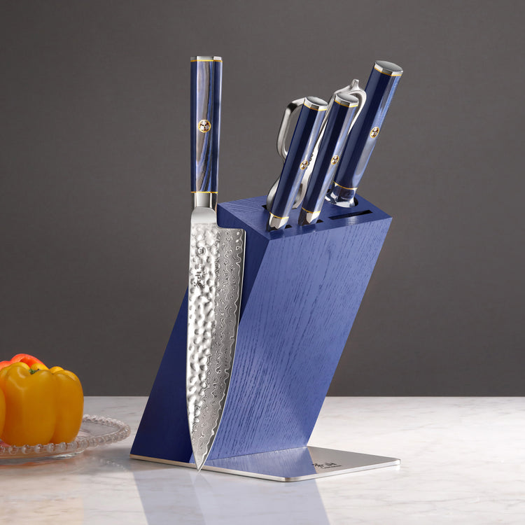 Six-piece knife set with hammered blades and blue handles in a matching blue angled wooden block on a marble surface.