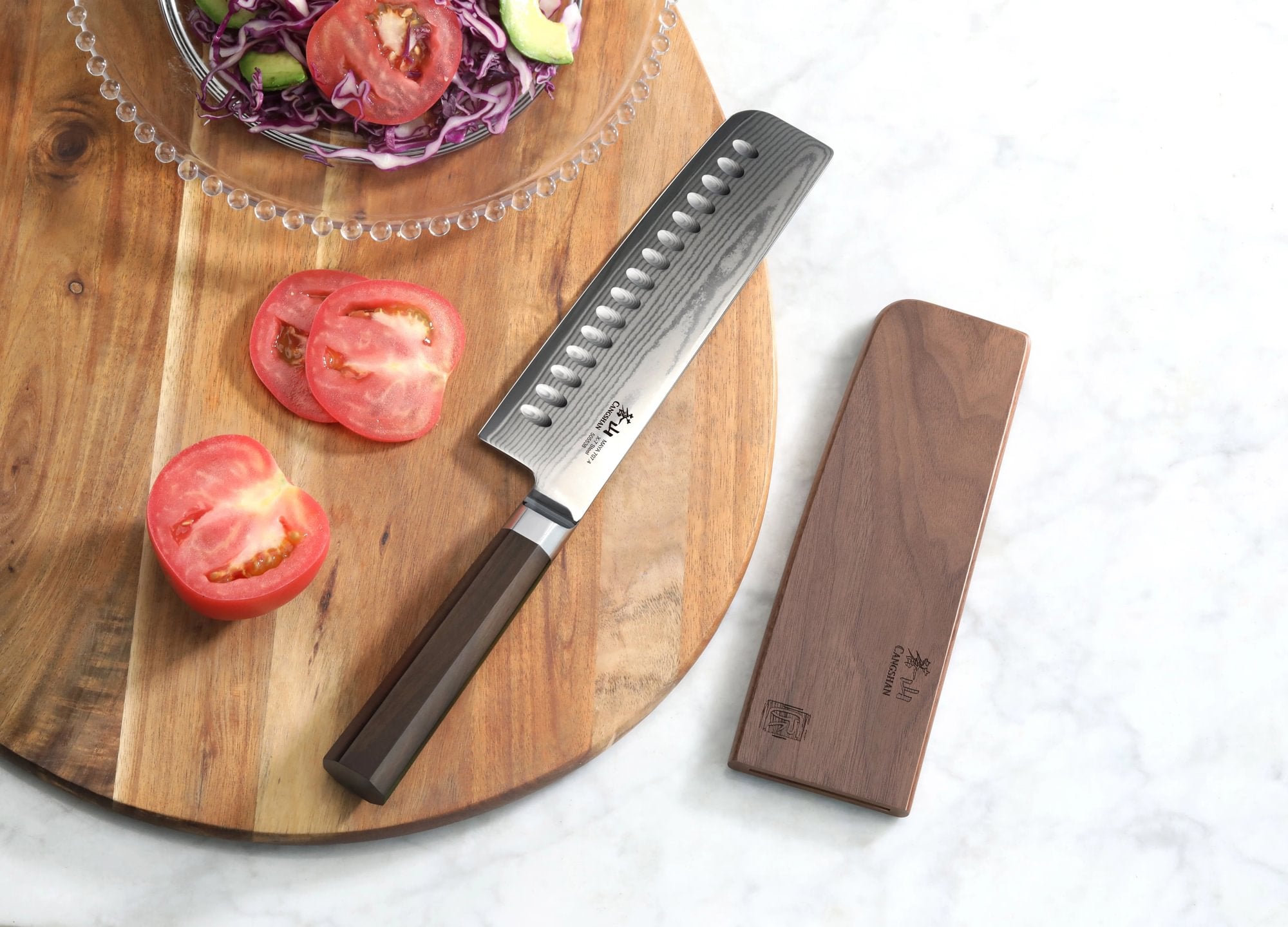 MAYA Series 7-Inch Nakiri Knife X-7 Damascus Steel on a cutting board next to a wooden sheath and sliced tomatoes.