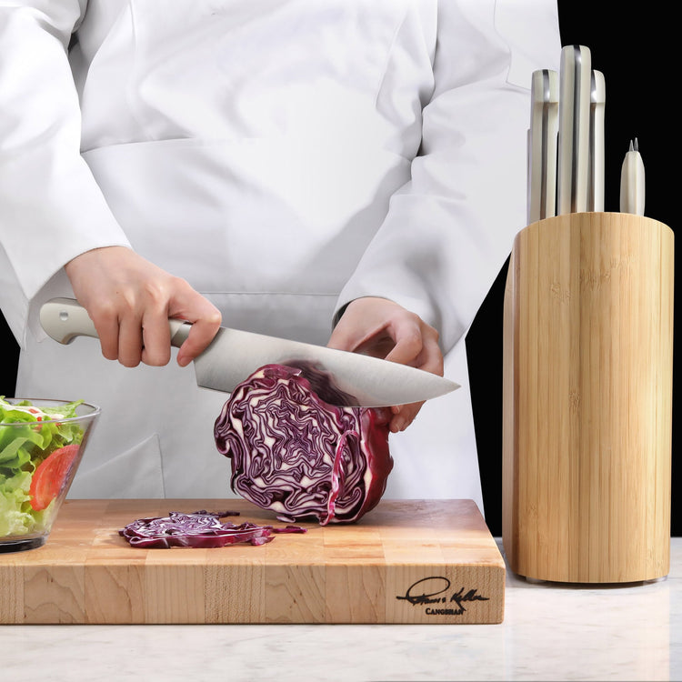 Person slicing red cabbage on a wooden cutting board next to a bamboo knife block with stainless steel knives.