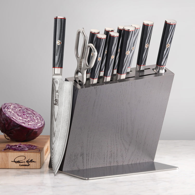 Knife block set with eight knives and kitchen shears in a dark wood block on a marble countertop.