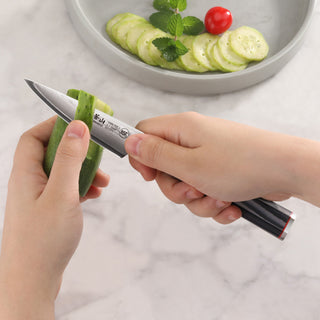 
                    
                      Hands peeling a cucumber with a small paring knife featuring a black handle and Damascus steel blade.
                    
                  