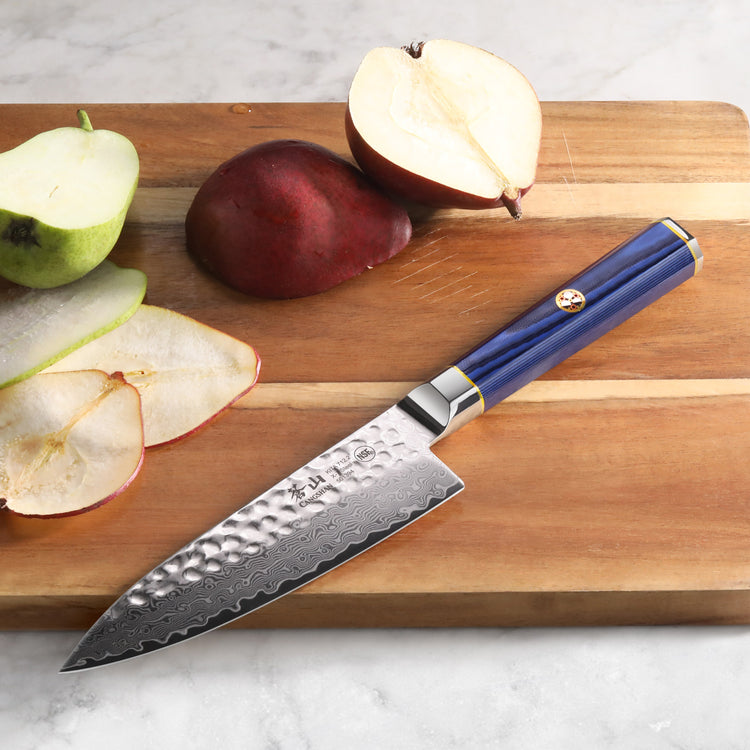 Chef knife with hammered Damascus steel blade and blue handle on wooden cutting board with sliced pears.