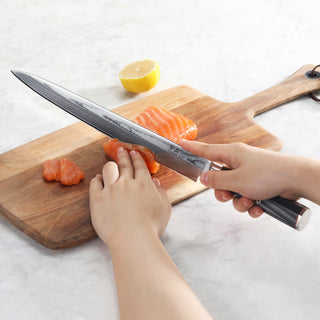 
                    
                      Hand holding a sashimi knife slicing raw salmon on a wooden cutting board with half a lemon in the background.
                    
                  