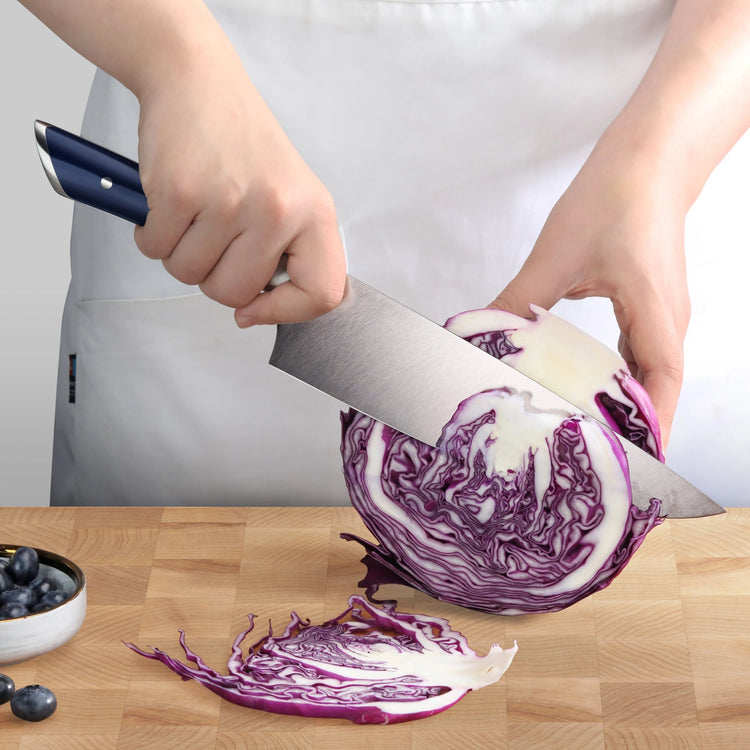 Person slicing a head of purple cabbage with a blue-handled chef's knife on a wooden cutting board.