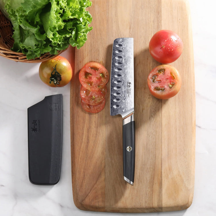 AIRA Series 5-Inch Nakiri Knife with patterned steel blade and black handle on a wooden cutting board with sliced tomatoes.