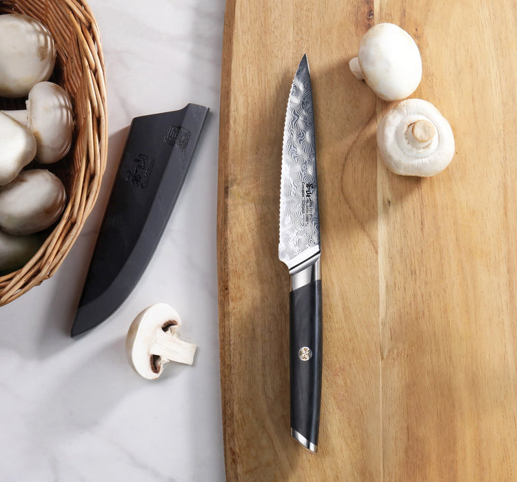 AIRA Series 5-Inch Serrated Utility Knife with 135-Layer Damax™ Steel on a wooden cutting board with mushrooms and a black