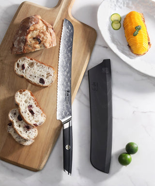 
                    
                      AIRA Series 9-Inch Bread Knife with Damax steel on a cutting board next to sliced bread and its black sheath.
                    
                  