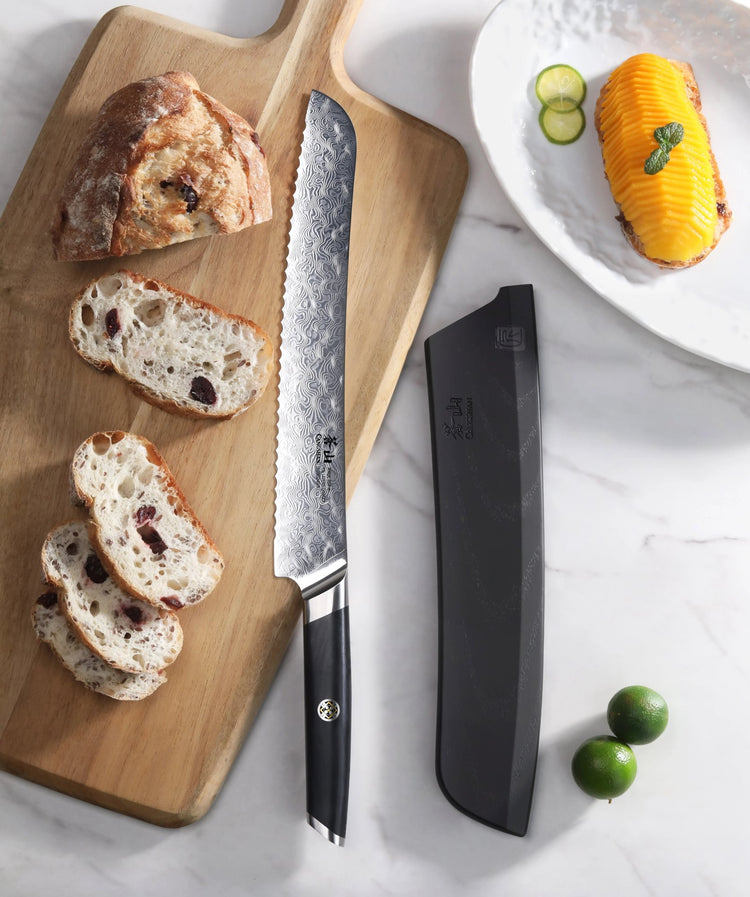 AIRA Series 9-Inch Bread Knife with Damax steel on a cutting board next to sliced bread and its black sheath.