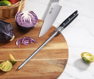 
                    
                      9-inch honing steel with black handle and knife on wooden cutting board next to sliced purple cabbage and green tomatoes.
                    
                  